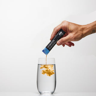 A hand pouring a Sküma HYDRATION.melisse stick into a glass of water