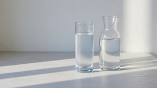 A misted glass of cold water beside a glass carafe on a pale counter in morning light