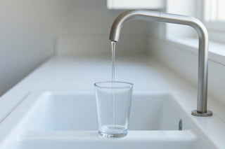 Water running from a brushed steel kitchen tap into a glass